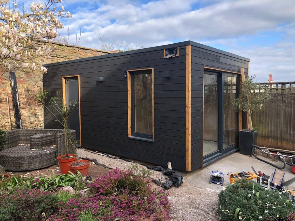 Black timber-clad garden room built on a patio surrounded by planting