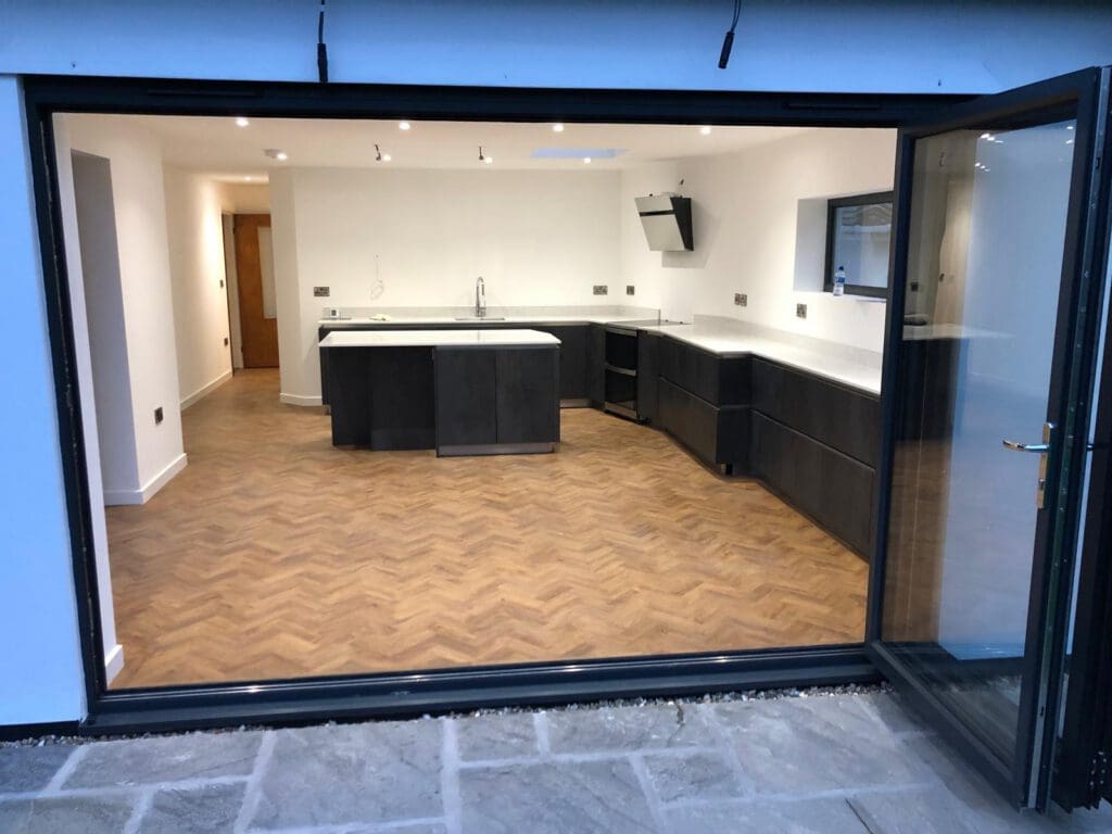 Modern kitchen with dark cabinets, white worktops and a central island opening onto the garden